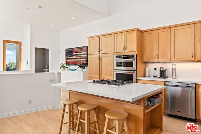 kitchen with a kitchen bar, appliances with stainless steel finishes, a center island, and light hardwood / wood-style floors