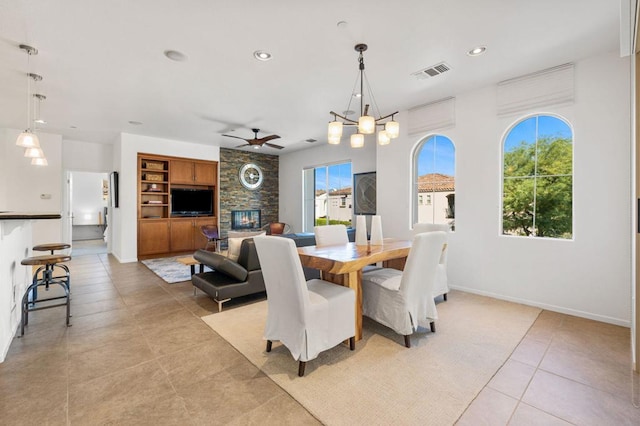 tiled dining area with built in shelves, a fireplace, a healthy amount of sunlight, and ceiling fan with notable chandelier