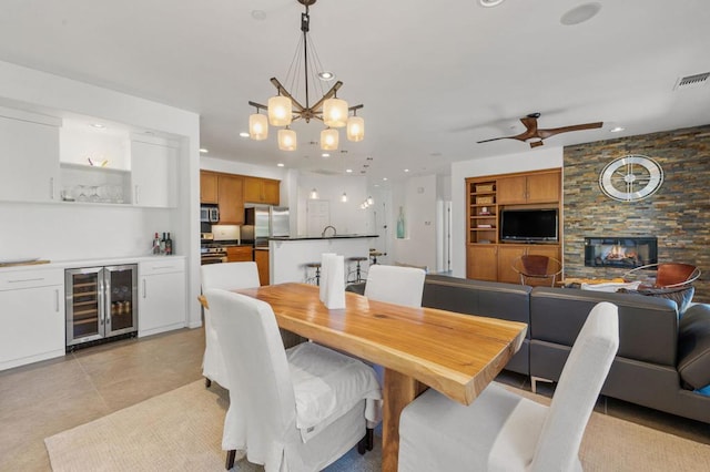 dining area featuring a fireplace, light tile patterned floors, ceiling fan with notable chandelier, and beverage cooler