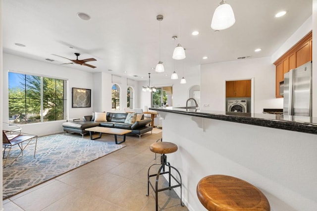 kitchen with pendant lighting, a kitchen breakfast bar, ceiling fan with notable chandelier, stainless steel fridge, and washer / clothes dryer