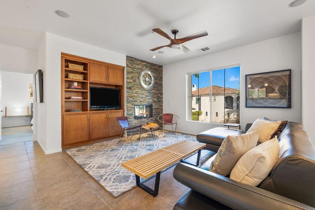 living room featuring ceiling fan, a stone fireplace, and light tile patterned floors