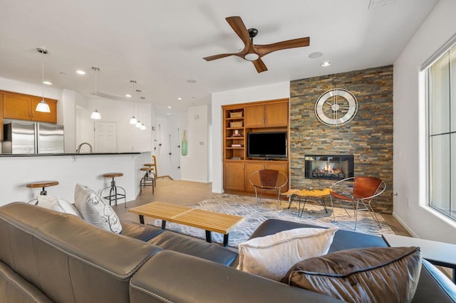 living room with ceiling fan, a stone fireplace, and built in shelves