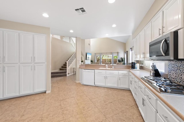 kitchen with lofted ceiling, backsplash, sink, white cabinetry, and stainless steel appliances