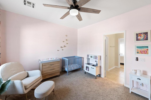 carpeted bedroom featuring a nursery area and ceiling fan