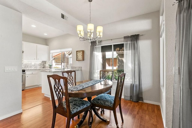 dining area with a notable chandelier, light wood-type flooring, sink, and a wealth of natural light