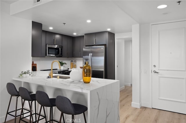 kitchen featuring kitchen peninsula, a kitchen breakfast bar, light stone countertops, light wood-type flooring, and stainless steel appliances