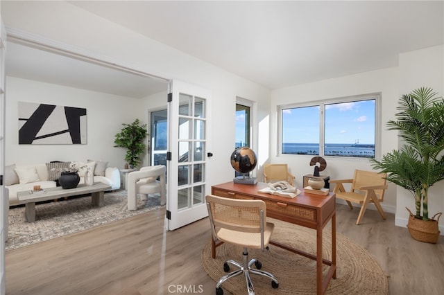 office area with french doors, hardwood / wood-style floors, and a water view