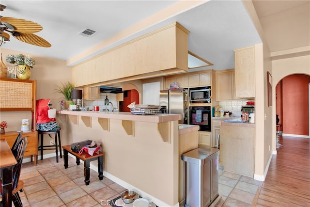 kitchen with appliances with stainless steel finishes, kitchen peninsula, decorative backsplash, and a kitchen breakfast bar