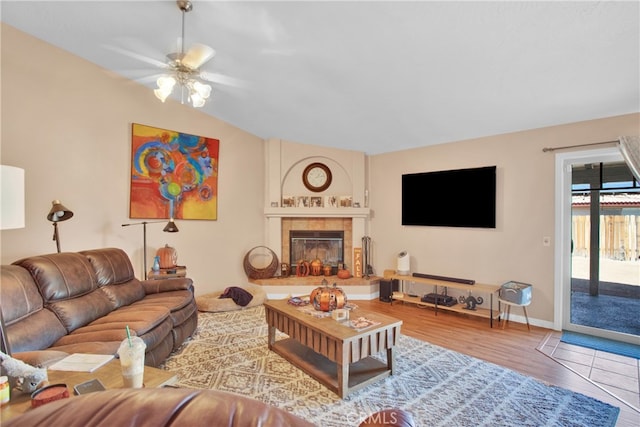 living room featuring vaulted ceiling, wood-type flooring, a tile fireplace, and ceiling fan