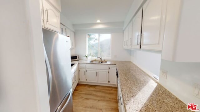 kitchen featuring stainless steel refrigerator, sink, light stone counters, white cabinets, and light wood-type flooring