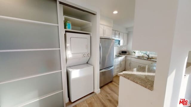 kitchen featuring light hardwood / wood-style floors, sink, white cabinets, stacked washer and dryer, and stainless steel refrigerator