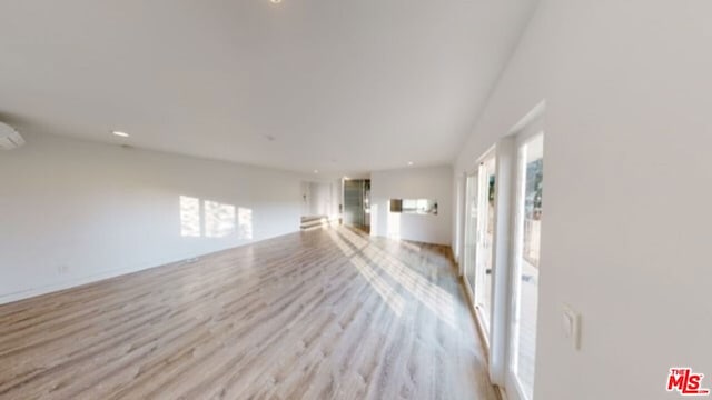 unfurnished living room featuring light hardwood / wood-style flooring and a wall unit AC