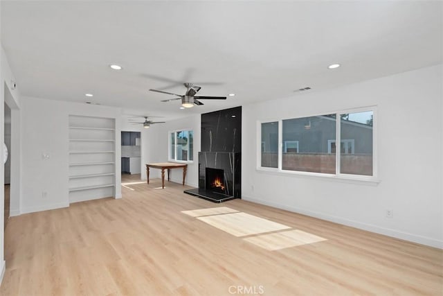 unfurnished living room with ceiling fan, built in shelves, light wood-type flooring, and a large fireplace