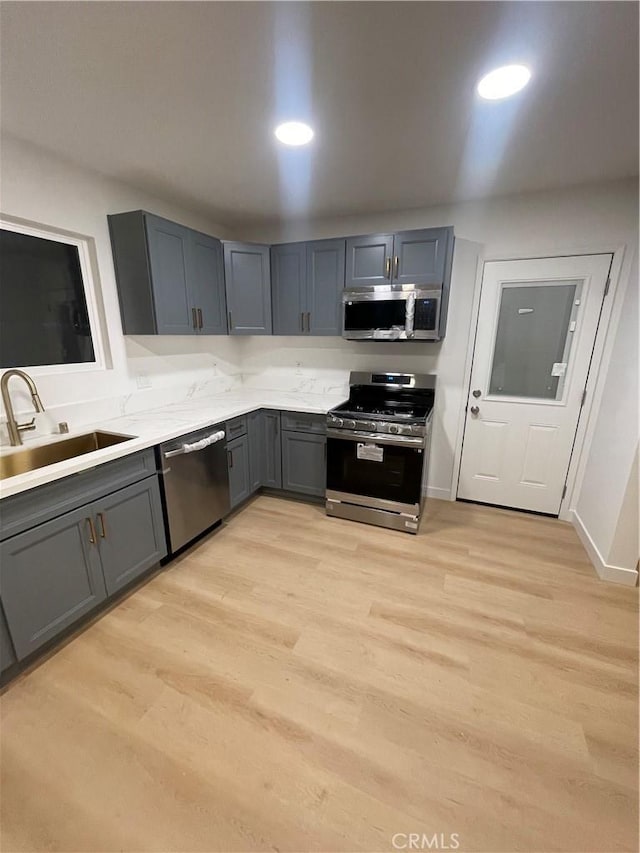 kitchen with gray cabinets, stainless steel appliances, light hardwood / wood-style flooring, and sink