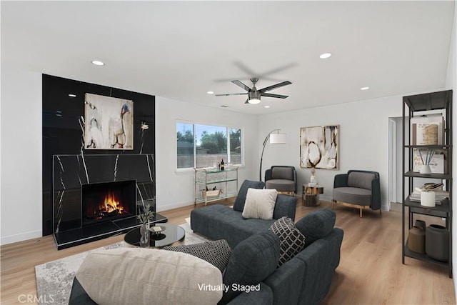 living room featuring ceiling fan, light hardwood / wood-style flooring, and a tiled fireplace