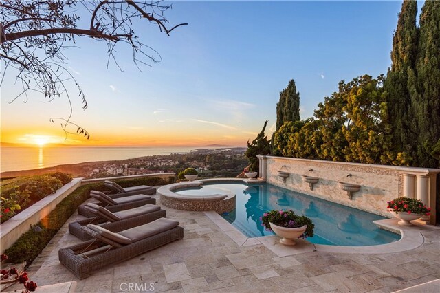 pool at dusk with a patio area, an in ground hot tub, and a water view