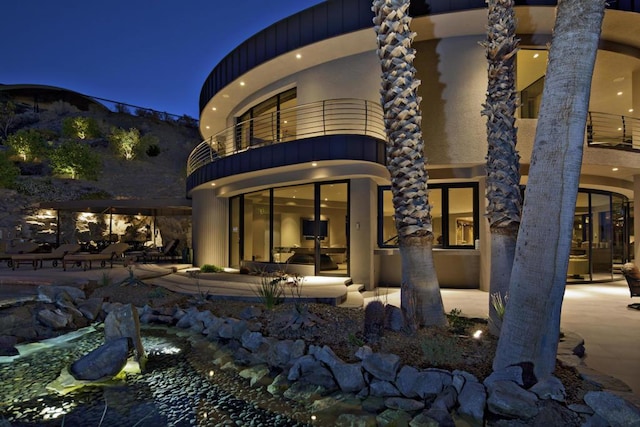 back house at night featuring a balcony and a patio area