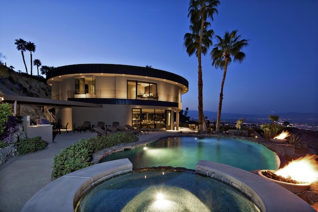 pool at dusk with an in ground hot tub and a patio area