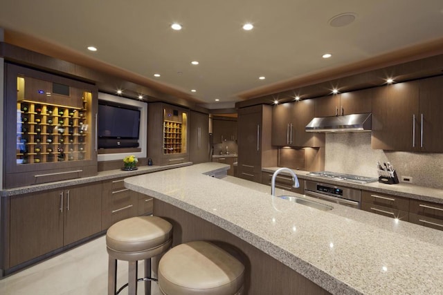 kitchen with a kitchen breakfast bar, sink, tasteful backsplash, light stone countertops, and stainless steel appliances