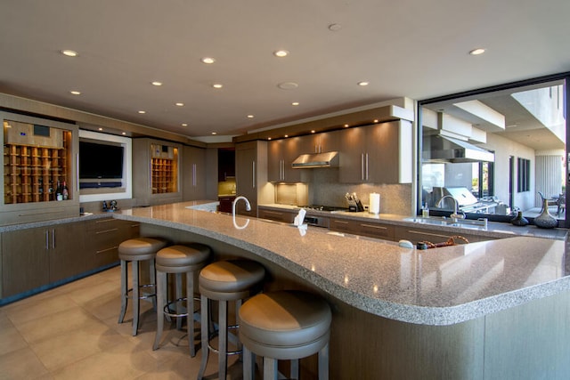 kitchen featuring stainless steel gas stovetop, tasteful backsplash, sink, a breakfast bar, and light stone counters