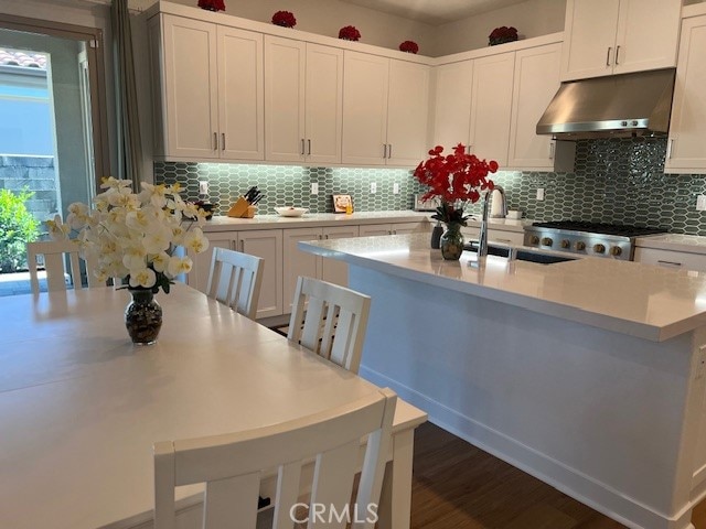 kitchen with decorative backsplash, stainless steel range, a center island with sink, and white cabinets