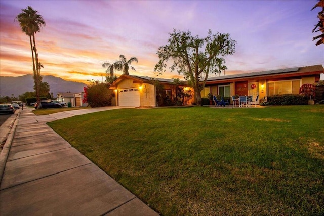 ranch-style house with solar panels, a garage, a yard, and a mountain view