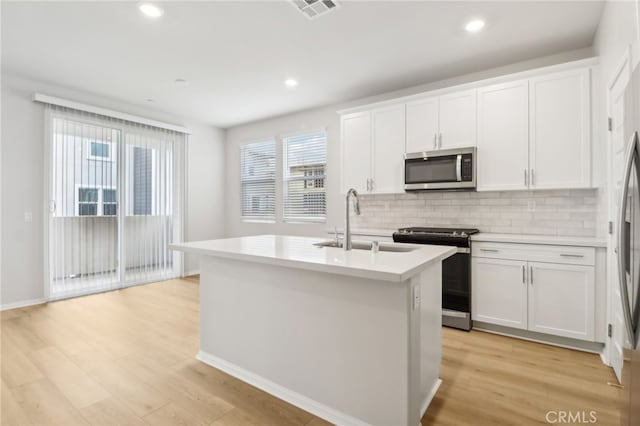 kitchen with appliances with stainless steel finishes, light hardwood / wood-style flooring, white cabinetry, and an island with sink