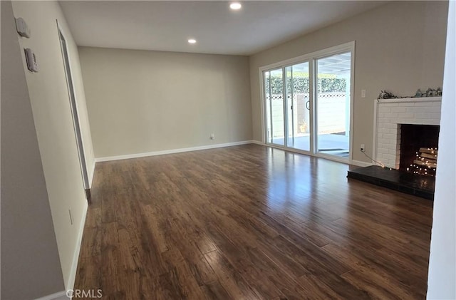 unfurnished living room featuring a brick fireplace and dark wood-type flooring