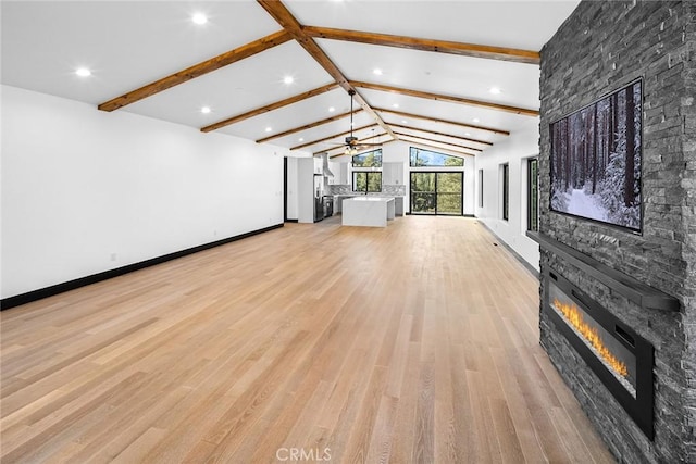 unfurnished living room with a stone fireplace, lofted ceiling with beams, ceiling fan, and light hardwood / wood-style floors