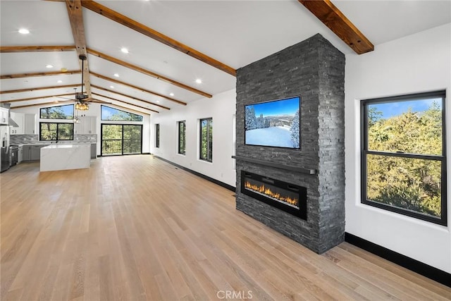 unfurnished living room featuring vaulted ceiling with beams, light hardwood / wood-style floors, a stone fireplace, and ceiling fan