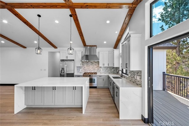 kitchen featuring wall chimney exhaust hood, stainless steel appliances, sink, beamed ceiling, and a center island