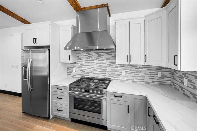 kitchen with wall chimney exhaust hood, light stone counters, decorative backsplash, appliances with stainless steel finishes, and light wood-type flooring