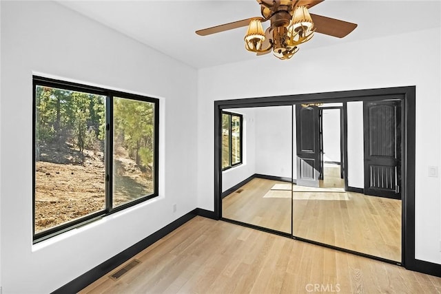 unfurnished bedroom featuring a chandelier, light hardwood / wood-style floors, multiple windows, and a closet