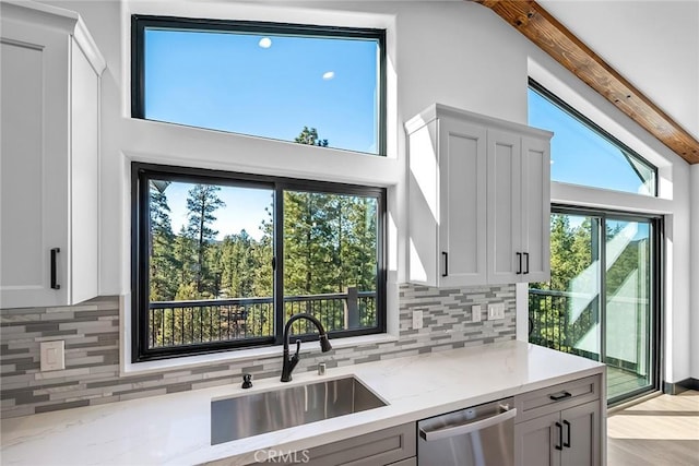 kitchen with light stone countertops, backsplash, stainless steel dishwasher, sink, and light hardwood / wood-style flooring