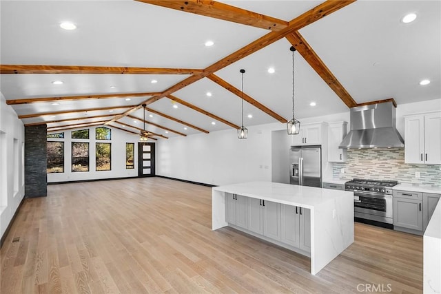 kitchen with appliances with stainless steel finishes, light wood-type flooring, a spacious island, wall chimney range hood, and decorative light fixtures