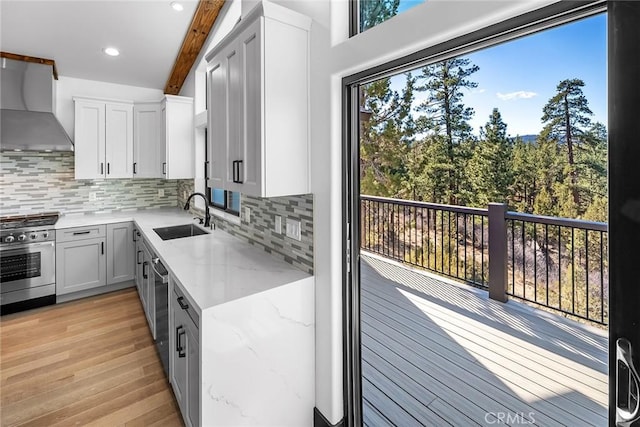 kitchen with sink, a healthy amount of sunlight, stainless steel appliances, wall chimney range hood, and beamed ceiling