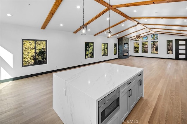 kitchen featuring lofted ceiling with beams, decorative light fixtures, light wood-type flooring, a large island, and light stone counters