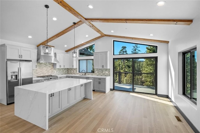 kitchen with pendant lighting, a center island, wall chimney range hood, light hardwood / wood-style flooring, and appliances with stainless steel finishes