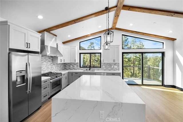 kitchen featuring stainless steel appliances, wall chimney range hood, lofted ceiling with beams, decorative light fixtures, and decorative backsplash