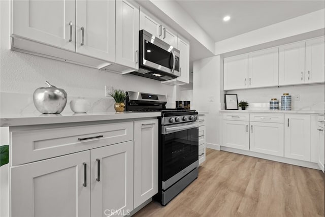 kitchen featuring appliances with stainless steel finishes, light hardwood / wood-style flooring, white cabinetry, and light stone countertops