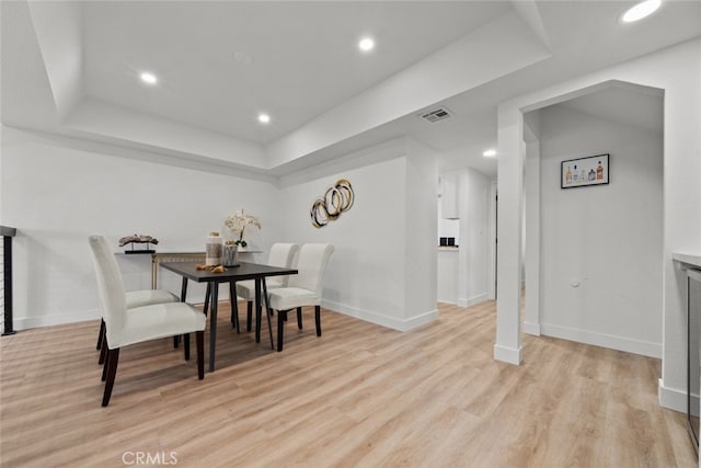 dining area with light hardwood / wood-style floors and a tray ceiling