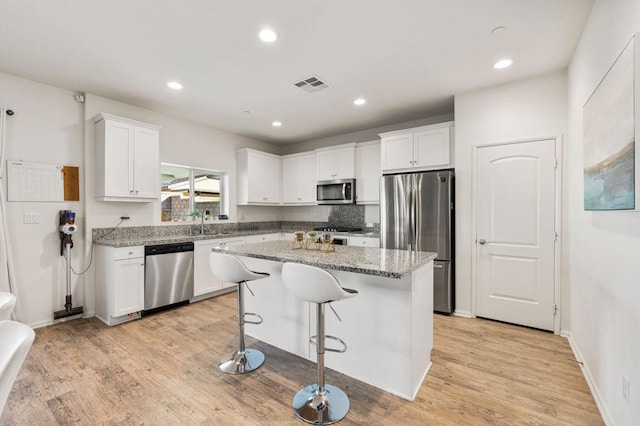 kitchen featuring white cabinets, a center island, light stone countertops, and appliances with stainless steel finishes