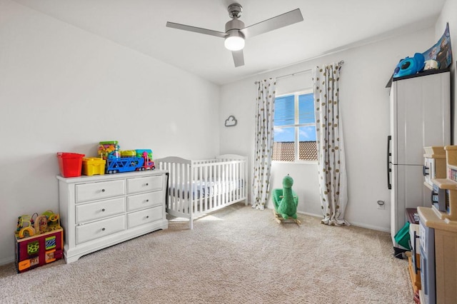 carpeted bedroom with ceiling fan and a nursery area