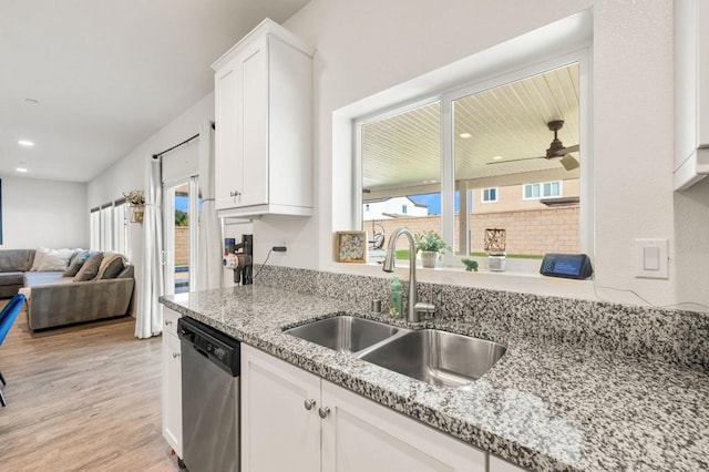 kitchen with light wood-type flooring, light stone counters, stainless steel dishwasher, sink, and white cabinetry