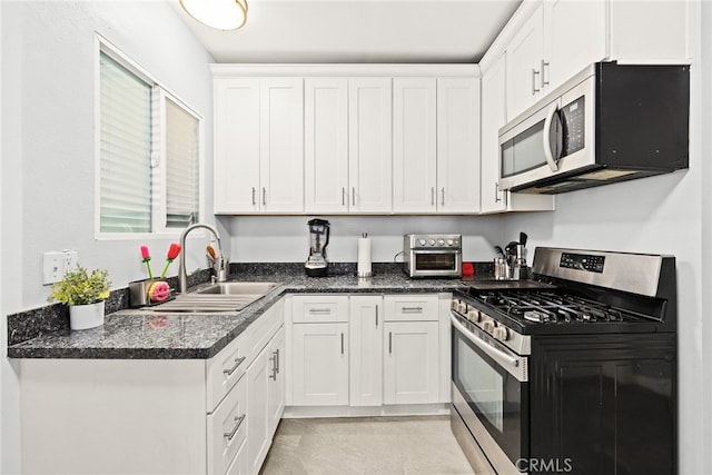 kitchen with white cabinetry, appliances with stainless steel finishes, sink, and dark stone counters