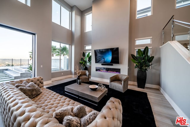 living room featuring a healthy amount of sunlight, light wood-type flooring, and a towering ceiling