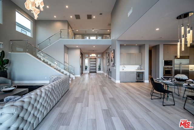 entryway featuring an inviting chandelier, sink, wine cooler, light hardwood / wood-style flooring, and a towering ceiling