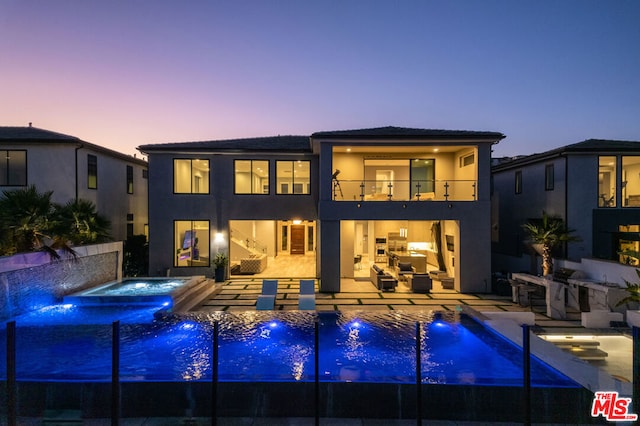 back house at dusk with exterior kitchen, a pool with hot tub, pool water feature, a balcony, and a patio