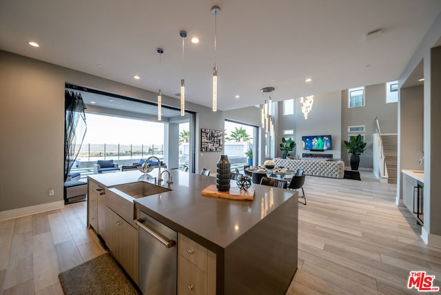 kitchen featuring stainless steel dishwasher, light wood-type flooring, an island with sink, and a wealth of natural light