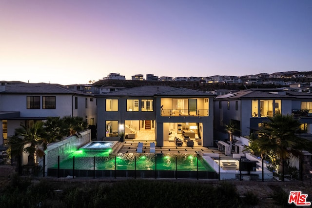 back house at dusk with a pool with hot tub, a patio area, and a balcony